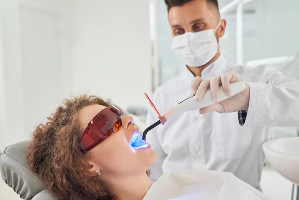 patient receiving professional teeth whitening treatment with dental curing light